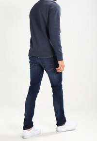 Sudadera azul marino de mangas largas, combinada con jeans ajustados de color azul oscuro y zapatillas blancas. El conjunto presenta un diseño minimalista y un ajuste cómodo.