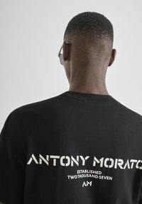 Camiseta de algodón negra con el texto "ANTONY MORATO" en blanco y con una tipografía moderna, costuras visibles y un diseño de cuello redondo.