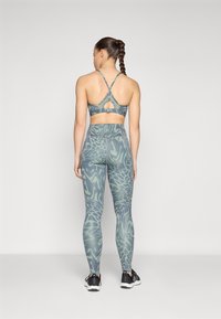 Completo di reggiseno sportivo e leggings con un motivo a vortice verde-blu. Il reggiseno presenta uno scollo a chiave sul retro e spalline incrociate. I leggings sono a vita alta.