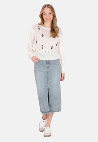 Pulover alb tricotat cu broderie florală, asortat cu o fustă din denim albastru deschis, cu fanta frontală, și adidași albi cu accente bej.
