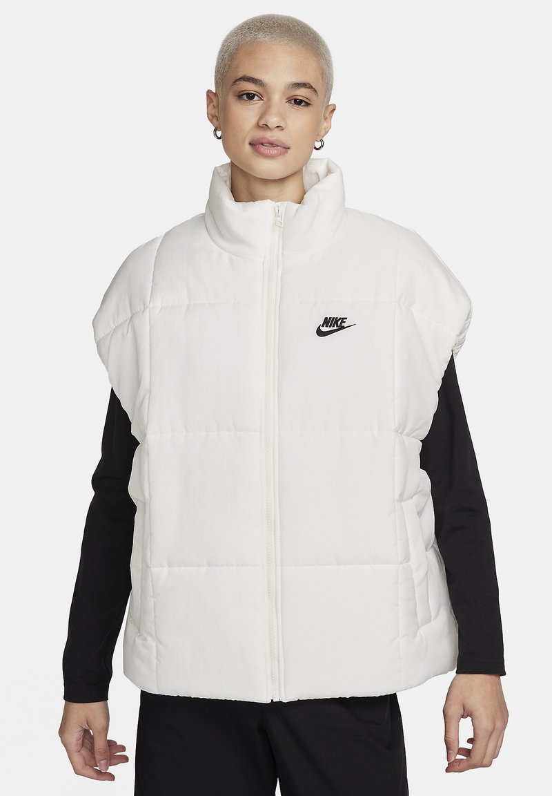 Chaleco inflable blanco con cuello alto, cierre de cremallera y logo negro de Nike en el pecho. Confeccionado en tela acolchada, con mangas cortas.