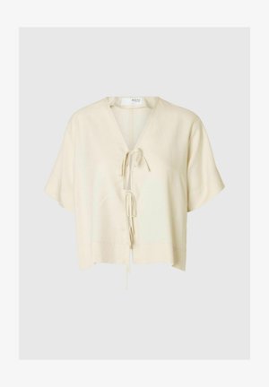 Blusa a maniche corte di colore crema con scollo a V e chiusura a nastro sul davanti. Tessuto morbido con una vestibilità rilassata e orlo dritto.