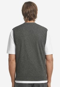 Grå ullväst med en figursydd design, ärmlös stil och ribbade kanter, bärs över en vit skjorta. Slät textur och klassisk form.