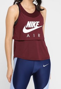 Crop top Nike Air in bordeaux, caratterizzato da una texture a coste e un grande logo bianco. Abbinato a leggings blu scuro con un logo discreto.