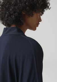 Indumento leggero di colore blu navy, con una texture morbida e un colletto, che mostra il profilo posteriore e laterale.