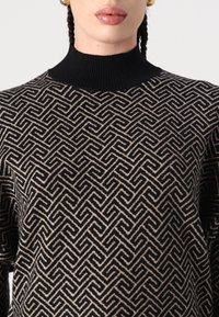 Pull noir et beige à motifs avec un col montant, présentant un design géométrique et une texture côtelée. Vue en gros plan du tissu.