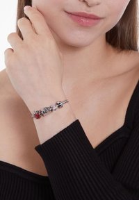 Zilveren armband met meerdere kleurrijke bedels, waaronder een rode, met unieke vormen en decoratieve accenten. Draagt op een blote pols.