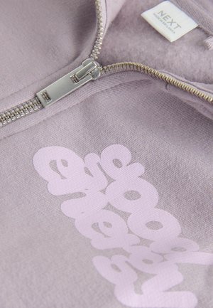 Light purple zip-up hoodie with silver zipper and partially visible white logo text, showing inside collar tag with brand name NEXT.
