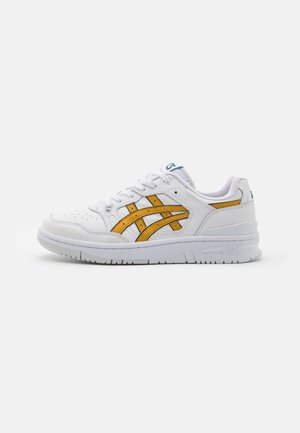 Baskets de sport blanches avec des bandes orange, des lacets et une semelle rembourrée, vues de côté sur un fond blanc uni.