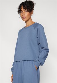 Sudadera corta azul con mangas raglán, confeccionada con una tela suave. Presenta un escote redondo y una cintura elástica, diseñada para un uso casual.