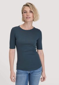 Strak, kortmouw teal shirt met een ronde halslijn en glad, rekbaar materiaal. Gecombineerd met lichtblauwe jeans.