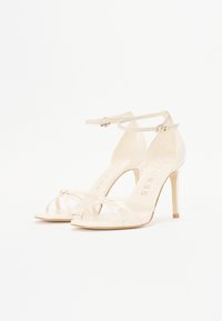 Clear high-heeled sandals with a transparent strap design, featuring a slender ankle strap and a knotted detail on the toe area.