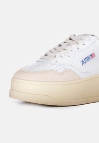 Sneaker bianco in pelle con sovrapposizione in camoscio beige, punta rotonda, lacci piatti e suola imbottita. Presenta un piccolo logo con un accento della bandiera americana.