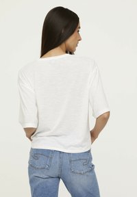 T-shirt blanc à manches courtes avec une coupe décontractée, dotée d'un col rond et d'un tissu légèrement texturé, assortie à un jean bleu clair.