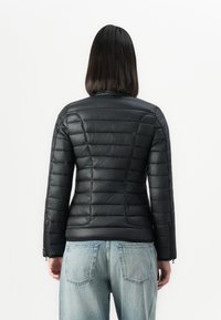 Giacca a vento nera con un design aderente, caratterizzata da texture trapuntate e maniche lunghe. Abbinata a jeans in denim azzurro chiaro.