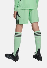 Groene voetbalshirt en -short met zwarte accenten, gecombineerd met zwarte voetbalschoenen en mintgroene sokken met zwarte strepen en een textuurdesign.