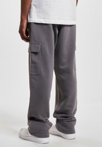 Gray sweatpants with a relaxed fit, featuring side cargo pockets and cuffed hems, paired with white sneakers. Soft fabric texture.