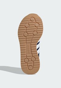 Gumeni potplat cipela sa teksturiranom, uzorčanom površinom i kružnim hvatištima, u svijetlosmeđoj boji, s utisnutim "adidas" pečatom blizu pete.