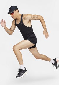 Schwarzes sportliches Tanktop und Shorts mit einem Nike-Logo, in Laufbewegung, trägt eine schwarze Mütze und reflektierende Sonnenbrille, schwarz-weiße Sneaker.