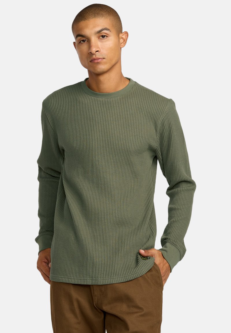 Langärmliges, olivgrünes Waffelstrickshirt mit Rundhalsausschnitt und Rippstruktur. Verfügt über ein dezentes Logoetikett nahe dem unteren Saum.