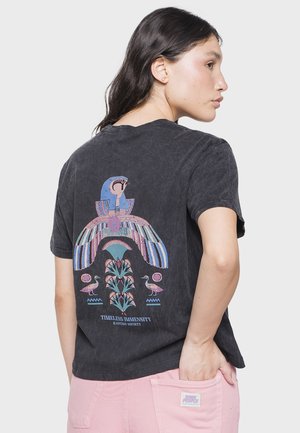Camiseta negra de manga corta con un gráfico colorido y detallado de un pájaro y plantas en la parte de atrás, con un corte relajado y textura suave.