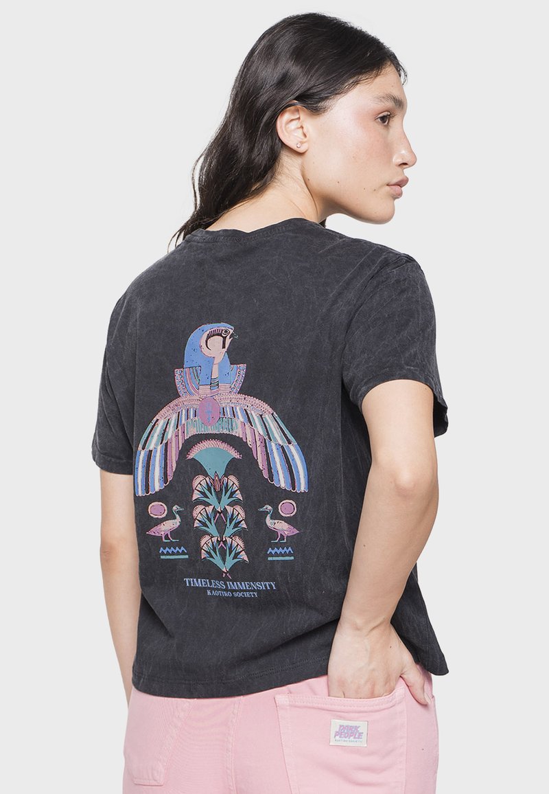 Camiseta negra de manga corta con un gráfico colorido y detallado de un pájaro y plantas en la parte de atrás, con un corte relajado y textura suave.