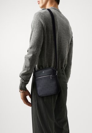 Bolso bandolera de cuero oscuro con un bolsillo con cremallera, que presenta un patrón grabado sutil. La correa es ajustable y se lleva colgada del hombro.