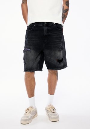 Czarne szorty dżinsowe z przetarciami, z dziurami i postrzępionymi brzegami. Noszone z szaro-białymi trampkami i białymi skarpetkami sięgającymi kostek.