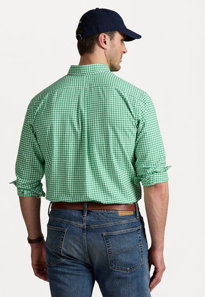 Chemise à carreaux vert et blanc avec des manches retroussées, assortie à un jean en denim bleu et une ceinture en cuir marron. Casquette navy sur la tête.