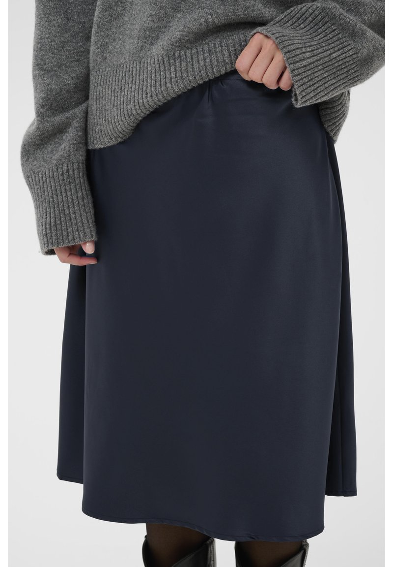 Jupe en satin bleu marine avec une texture lisse, une taille élastique et une coupe évasée, associée à un pull gris à côtes.