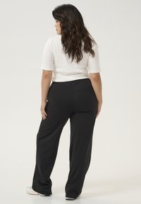 Pantalons larges noirs en tissu lisse avec une taille élastique, associés à un haut ajusté blanc à manches courtes. Design minimaliste.