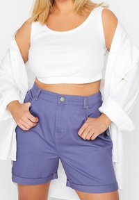 Fialové denimové šortky s vysokým pasem, ohrnutým lemem a předními kapsami. Spárované s bílým zkráceným topem a oversize bílou košilí.