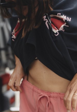 Czarny t-shirt z nadrukiem graficznym, krótkie rękawy, lekko podniesiony, odsłaniający brzuch, w połączeniu z luźnymi różowymi szortami ze ściągaczem.