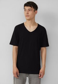 Czarna koszulka V-neck wykonana z miękkiego materiału, z krótkimi rękawami i luźnym krojem, w połączeniu z jasnoszarymi dżinsami.