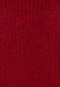 Gros plan sur un tissu tricoté rouge avec un motif texturé et duveteux, comprenant des boucles et des mailles visibles.