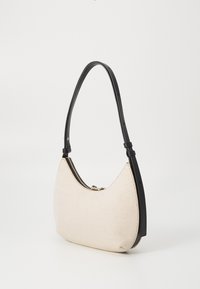 Μπεζ υφασμάτινη τσάντα ώμου με μαύρη δερμάτινη λαβή, καμπυλωτό σχήμα και χρυσές λεπτομέρειες στο φερμουάρ στην κορυφή. Λείο υφή, μινιμαλιστικός σχεδιασμός.