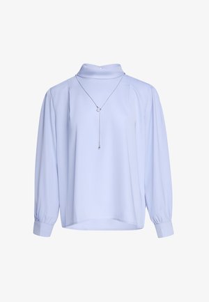 Hellblaue Bluse mit langen Ärmeln und hohem Kragen sowie plissierten Schultern, kombiniert mit einer dünnen silbernen Halskette mit zwei kleinen Anhängern.