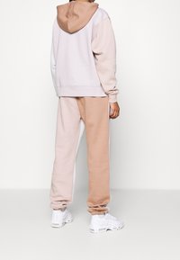 Huvtröja i ljus mauve med beige accenter, matchande med beige sweatpants. Tyget verkar mjukt med ribbade muddar och midja.