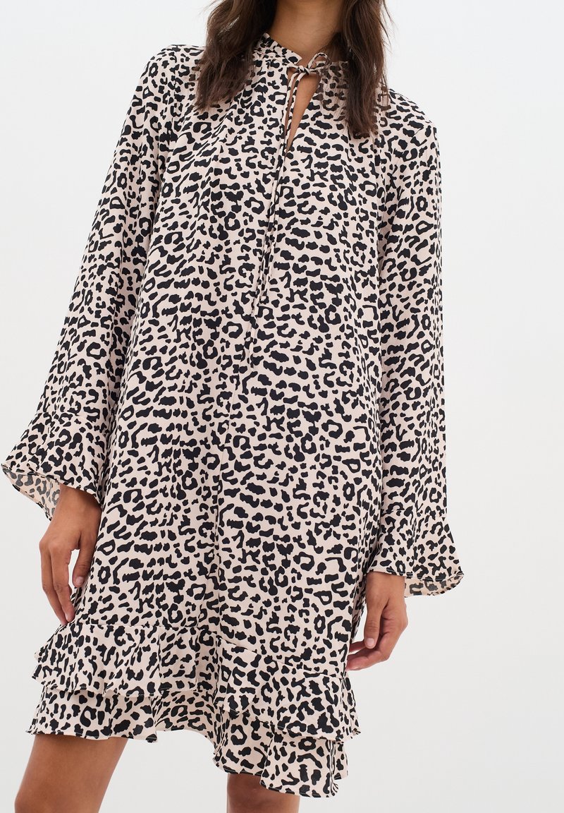 Mekko, jossa on leopardikuosi, kevyeistä kankaista valmistettu, sidottava kaula-aukko, pitkät hihat ja kerroksellinen röyhelöhelma. Värimaailma: beige ja musta.