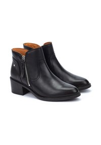 Botas de tobillo de cuero negro con puntera afilada, cremallera lateral y un bajo tacón cuadrado. El interior presenta un forro marrón claro para crear contraste.
