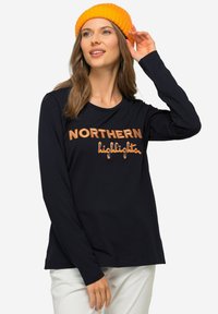 Granatowa koszulka z długim rękawem z haftem "NORTHERN highlights" w pomarańczowym kolorze. Miękki materiał, luźny fason, projekt z okrągłym dekoltem. Połączona z pomarańczową czapką beanie.