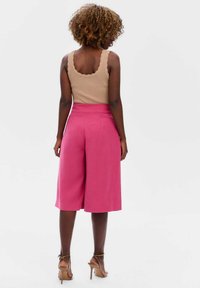Roze culotte-broeken met een gladde textuur, hoge taille en brede pijpen. Gepaard met een ribbelachtig tanktop met een gegolfde halslijn in beige.