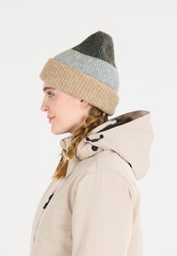 Villa beanie, jolla on kolmiomainen muoto, jossa on vaaleanharmaa, tummanharmaa ja beige värimaailma; ribattu pinta reunassa.