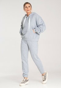 Szary hoodie z kapturem i białymi sznurkami, w luźnym kroju, z bocznymi kieszeniami, połączony z dopasowanymi spodniami dresowymi. Teksturowany materiał.