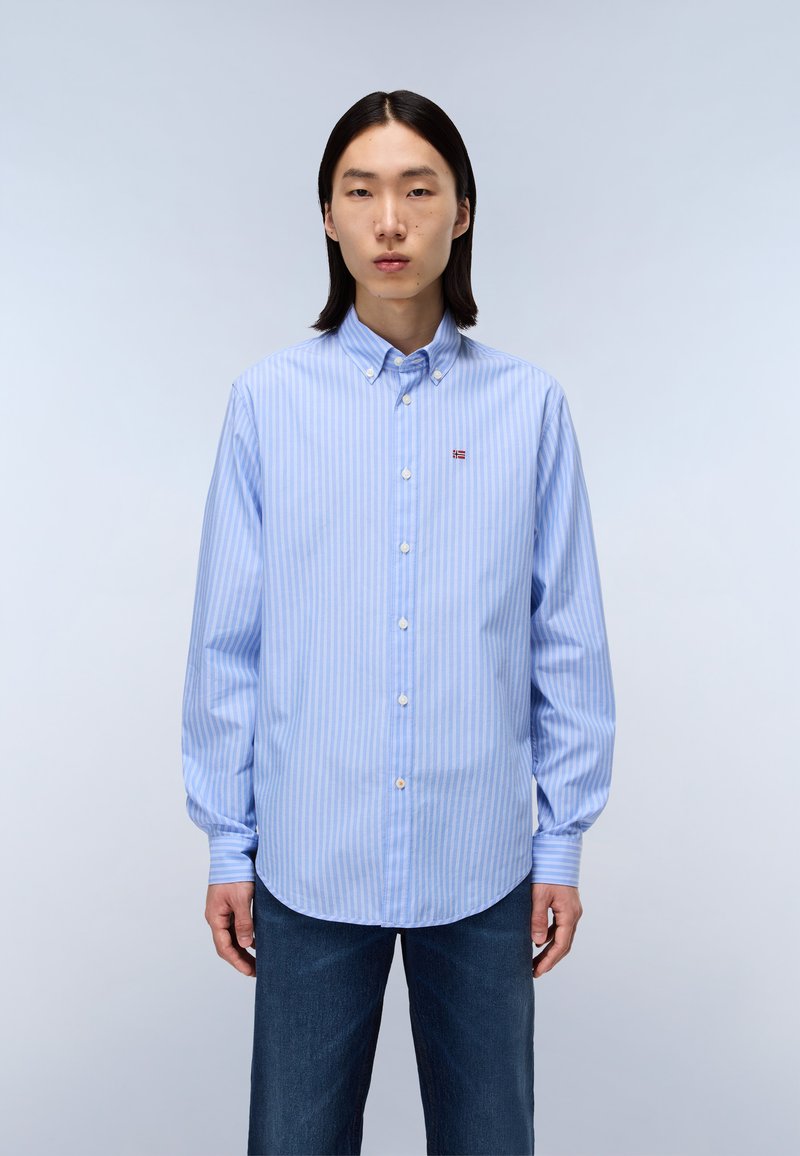 Chemise boutonnée rayée bleu clair avec col, manches longues et ourlet arrondi. Petit détail de logo sur la poitrine. Coupe classique.