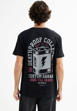 Camiseta de algodón negra con un diseño gráfico de una batería que incluye el texto: "Colección a prueba de muerte," "Garaje personalizado," y acentos de relámpago.