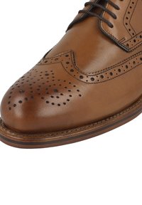 Scarpe eleganti in pelle marrone con design brogue, texture liscia, punta arrotondata e perforazioni dettagliate lungo la parte superiore e laterale.