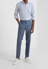 Camicia azzurra a righe con maniche arrotolate, abbinata a pantaloni grigi blu su misura e sneakers bianche. Outfit semplice con linee pulite.