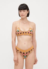 Háčkovaná bikiny súprava so šnurovaným topom a vysokým pásom, dostupná v niekoľkých farbách vrátane hnedej, oranžovej, ružovej a zelenej. Štruktúrovaný dizajn.