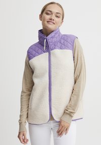 Vesta matlasată cu partea superioară mov și partea inferioară din fleece crem, având un guler înalt, închidere cu fermoar și detalii de trim violet.